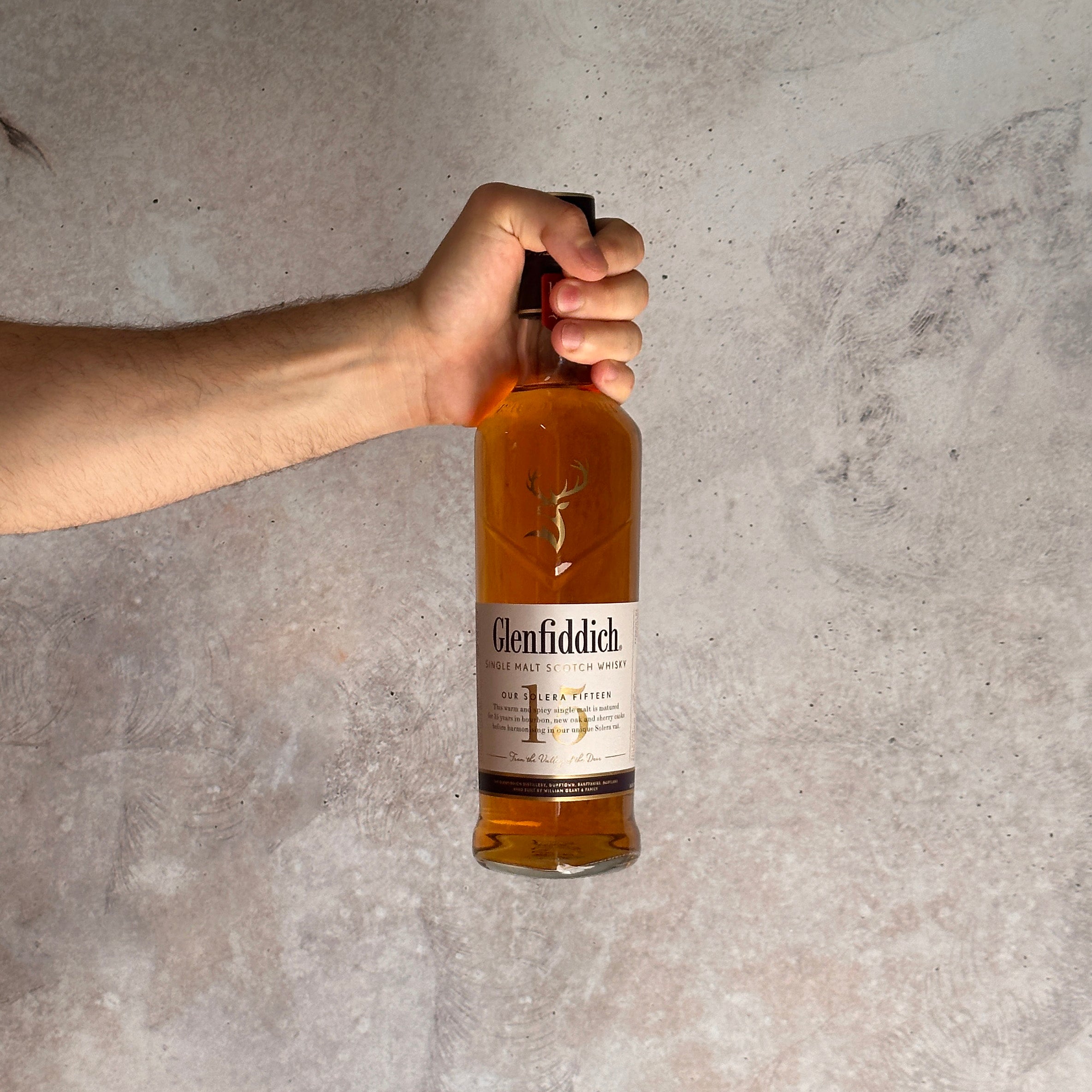 Hand holding a Glenfiddich whisky bottle against a gray background