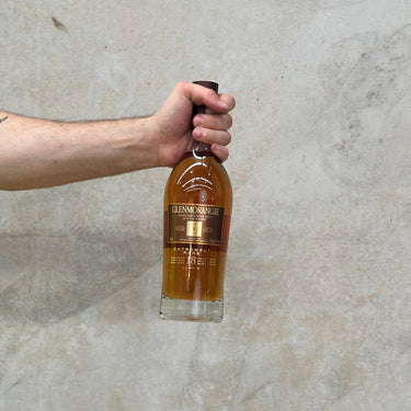 A hand holding a bottle of Glenmorangie 18 Year Old Extremely Rare Whisky against a grey background.