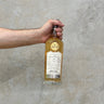 A hand holding a bottle of Caol Ila Gordon & Macphail 17 Year Old Japanese Exclusive - Cask Strength Whisky with a yellow label, against a grey concrete background.