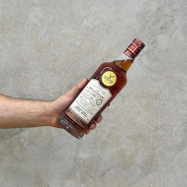 A hand holding a bottle of Gordon & Macphail Connoisseurs Choice Hermitage Cask 2007 Whisky against a grey background.