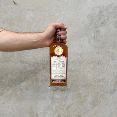 A bottle of Gordon & Macphail Connoisseurs Choice Sassicaia Cask Whisky held in hand against a grey background.