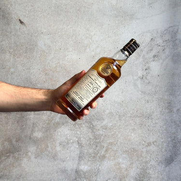 Hand holding a bottle of Gordon Macphail whiskey against a gray concrete background