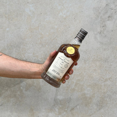 A hand holding a bottle of Gordon & Macphail Connoisseurs Choice Mortlach 1988 Whisky against a grey concrete background.
