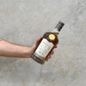 A hand holding a bottle of Gordon & Macphail Connoisseurs Choice Mortlach 1988 Whisky against a grey concrete background.