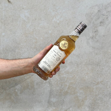 A bottle of Gordon & Macphail Connoisseurs Choice Tomatin 1990 whisky being held by a hand against a grey background.