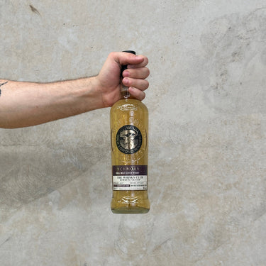 A hand holding a bottle of Inchmoan 2007 American Oak Whisky with a smoky campfire, vanilla custard, and toasted coconut flavour description.