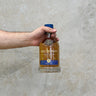 A hand holding a bottle of Kilchoman 100% Islay 12th Edition Whisky against a grey concrete background.