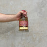 A hand holding a bottle of Kilchoman Casado Whisky with a concrete background.