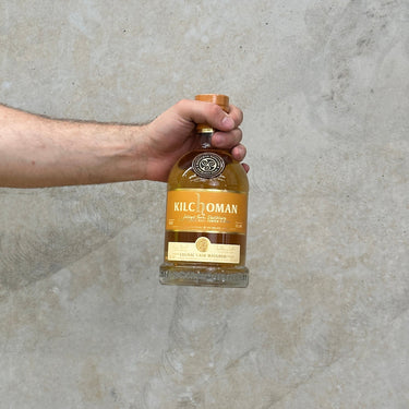 A hand holding a bottle of Kilchoman Special Release Cognac Cask whisky against a grey concrete background.