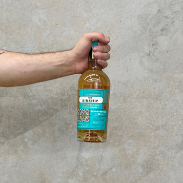 A hand holding a bottle of Kinship Bunnahabhain 1990 32 Year Old Whisky against a concrete wall