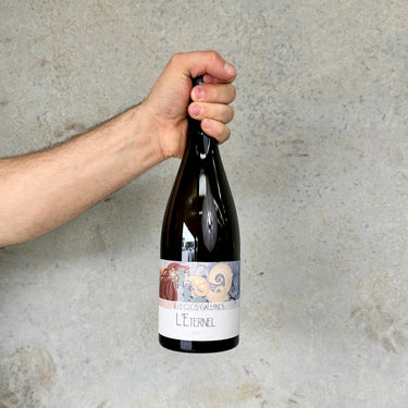 Hand holding a bottle of Léternel wine against a gray background