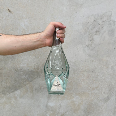 Hand holding a La Dama Tequila Blanco bottle against a concrete wall