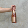 Hand holding a bottle of Laurenti sparkling wine against a gray concrete background