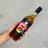 Bottle of Rum with a colorful label featuring a face design, held by a hand against a neutral background.