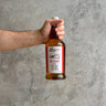 Hand holding a bottle of Longrow peated single malt scotch whisky against a gray concrete wall