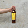 A hand holding a bottle of Macallan Edition 3 Whisky against a grey concrete background.