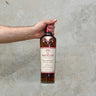 A hand holding a bottle of Macallan The Harmony Collection Intense Arabica Whisky against a textured background.