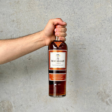 Hand holding a bottle of The Macallan whisky against a gray background