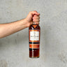 Hand holding a bottle of The Macallan whisky against a gray background