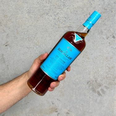 Hand holding a bottle of The Macallan whisky Edition No6 against a gray background