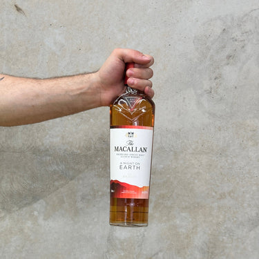 A hand holding a bottle of Macallan single malt Scotch whisky with a label that reads 'A Night On Earth - The Journey'.