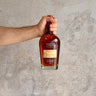 Hand holding a bottle of Maker's Mark bourbon against a gray concrete background