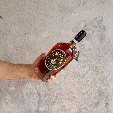 Hand holding a bottle of Michter's bourbon against a neutral background