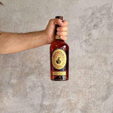 Hand holding a bottle of Michter's Limited Release Toasted Barrel Finish against a textured gray background