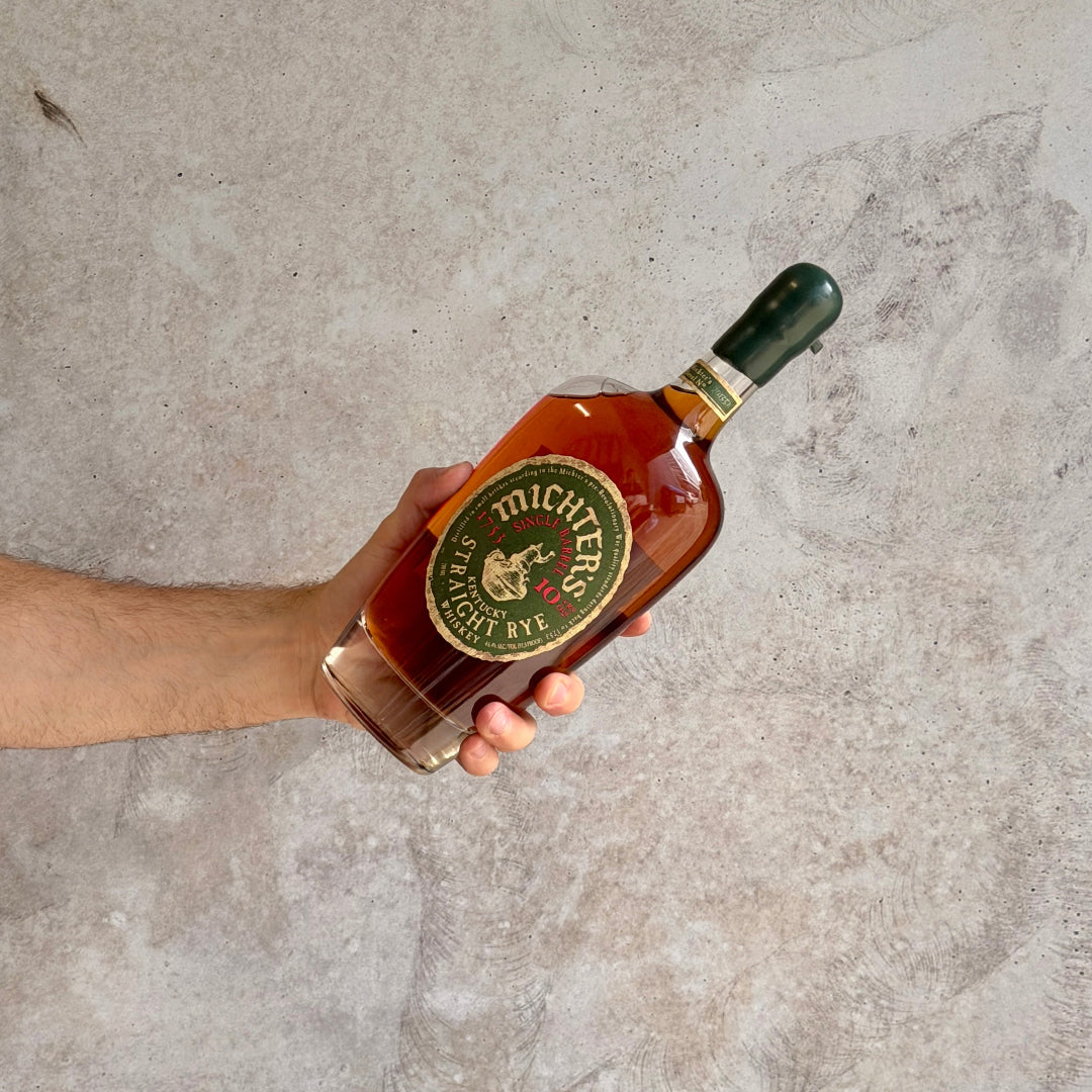 Hand holding a bottle of Michter's Straight Rye whiskey against a gray concrete background