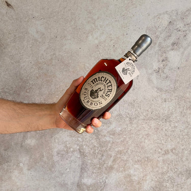 Hand holding a bottle of Michter's bourbon 20 Years Old against a gray concrete background