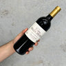 Hand holding a bottle of Mille Roses wine against a gray background