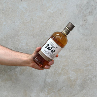 A hand holding a bottle of Miyagikyo 2021 Limited Edition Peated Whisky against a textured grey background.