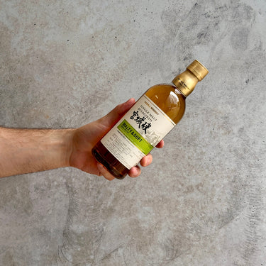 Hand holding a bottle of Nikka whisky against a gray concrete background