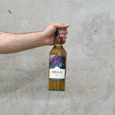 A hand holding a bottle of Oban Special & Rare Release 2022 10 Year Old Whisky against a grey background.