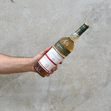 A hand holding a bottle of Craigellachie Hunter Laing Old Malt Cask 15 Year Old Whisky against a grey concrete background.