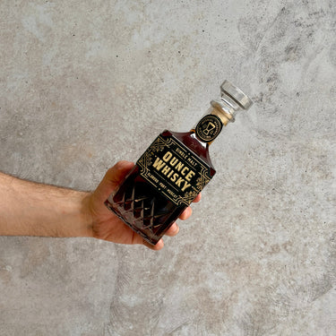 Hand holding a bottle of Ounce Single Malt Whisky against a concrete background