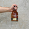 A hand holding a bottle of Overeem Man Of Promise 2022 Whisky with a label and clear liquid visible inside the bottle.