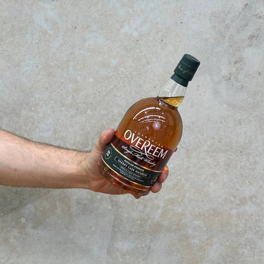 A hand holding a bottle of Overeem Sherry Cask Distillers Strength Whisky with a concrete background.
