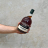A hand holding a bottle of Overeem Sherry Cask - Cask Strength Whisky with a label and cap, against a grey background.