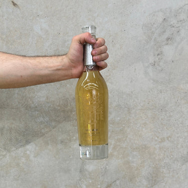 A hand holding a bottle of El Pandillo Pasote Extra Anejo tequila against a grey background.