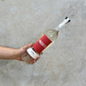 A hand holding a bottle of Pasote Reposado tequila with a red label, against a concrete background.