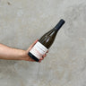 A hand holding a bottle of Domaine Passy Le Clou 2022 Chablis Wine against a textured grey background.