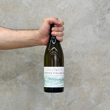 A hand holding a bottle of Domaine Passy Le Clou 2022 Petit Chablis with a label visible on the front.