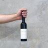 Hand holding a bottle of Confidence Wine against a concrete wall.
