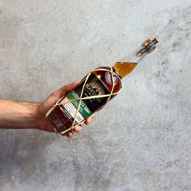 Hand holding a bottle of alcohol with a decorative string against a concrete background