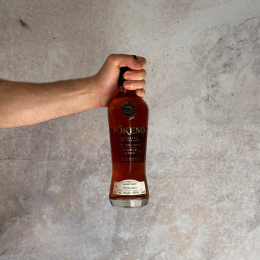 Hand holding a bottle of Pokéno Moscatel whisky against a textured gray background