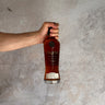 Hand holding a bottle of Pokéno Moscatel whisky against a textured gray background