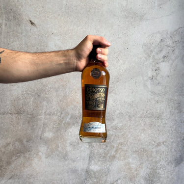 Hand holding a bottle of Pokeno whiskey against a gray background