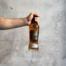 Hand holding a bottle of Pokeno whiskey against a gray background