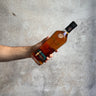 Hand holding a bottle of Pokeno Virgin Oak whiskey against a gray concrete background